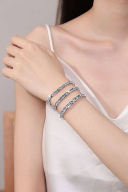 Close-up of a person wearing two silver bracelets on a neutral background