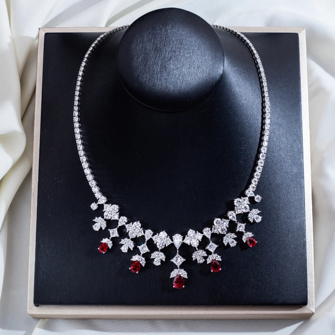 Diamanté necklace with red gemstones on a black stand against a white fabric background