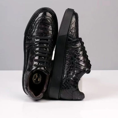 A pair of black crocodile-embossed leather sneakers shown from the side and top, standing on a white surface against a light gray background.