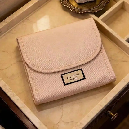 A light pink Gucci wallet with a textured canvas finish and a black-trimmed logo patch, resting inside a cream-colored marble drawer.