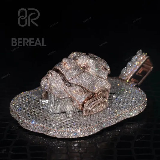 A heavily embellished lion head pendant covered in sparkling clear stones, with rose gold-toned metal details and a matching stone-encrusted collar, displayed on a black reflective surface. The BEREAL logo is visible in the upper left.