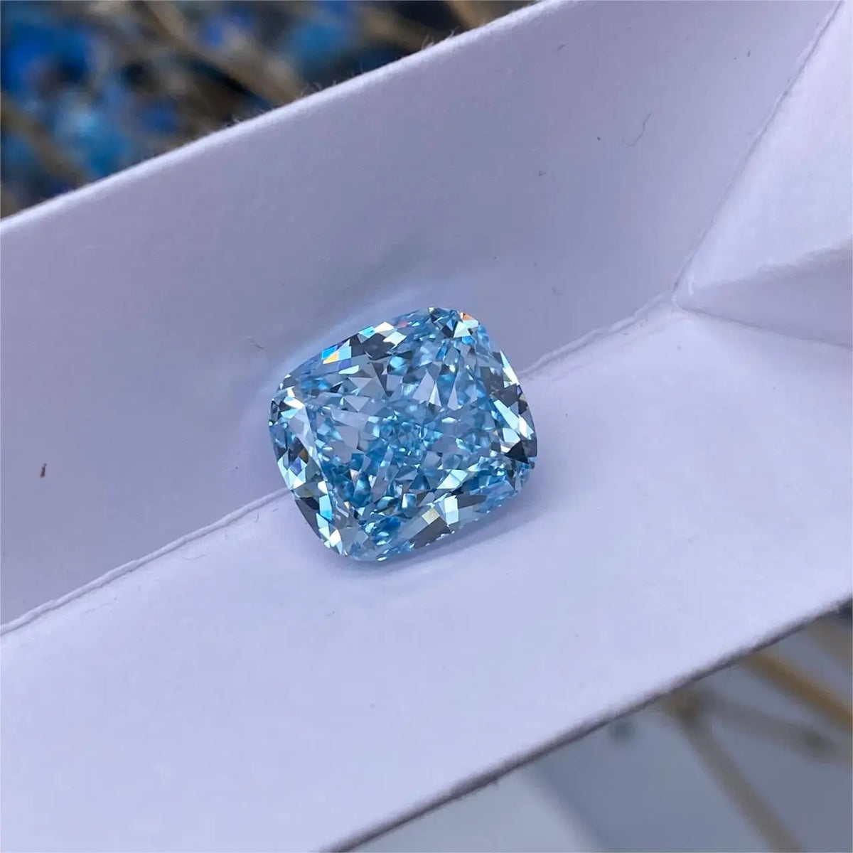 A cushion-cut light blue gemstone, likely a diamond, resting on a white textured surface.