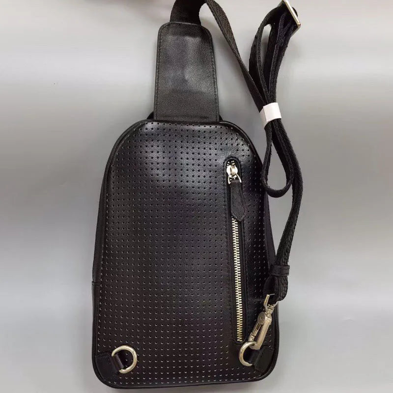 Black perforated leather crossbody bag with a front zip pocket, silver-tone hardware, and an adjustable shoulder strap, shown on a neutral gray background.