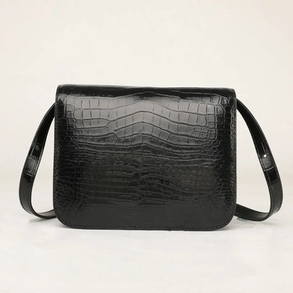 A black crocodile-embossed leather shoulder bag with a rectangular shape and a single strap, photographed against a plain off-white background.