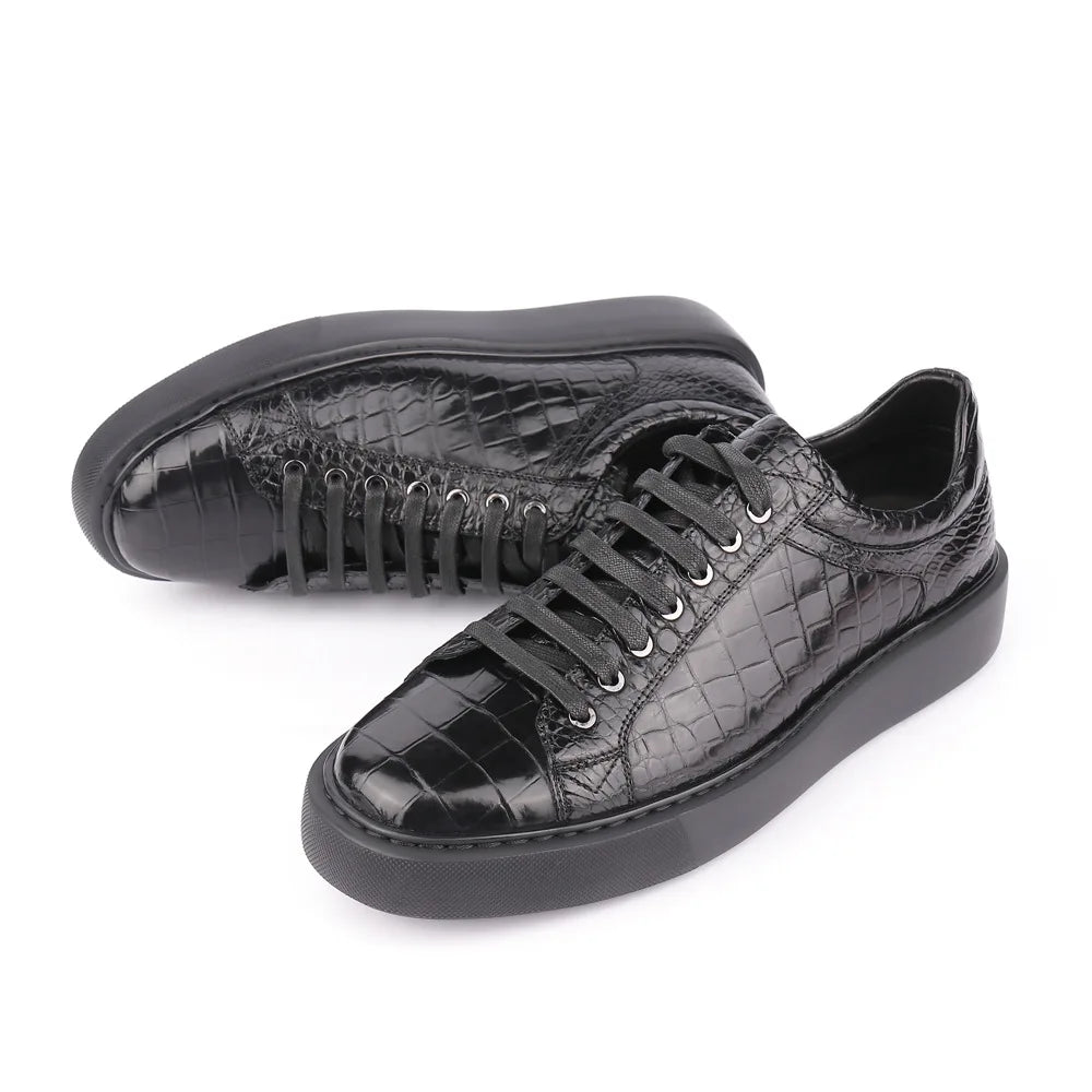 A pair of black low-top sneakers with a glossy crocodile-embossed leather upper, black laces, and thick black soles, displayed on a clean white background.