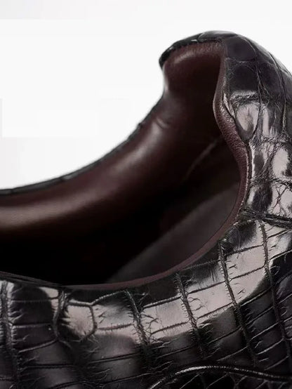 Close-up of a dark brown leather shoe with a crocodile-embossed texture and a smooth dark brown interior lining, shown against a plain white background.