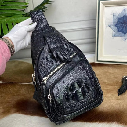 A black crocodile-embossed leather sling bag with multiple zippered compartments and a top handle, held by a white-gloved hand over a cowhide surface with a framed print in the background.