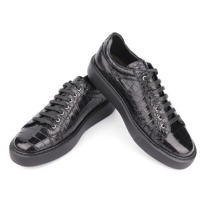 A pair of black low-top sneakers with a glossy crocodile-embossed texture, black laces, and chunky black soles, displayed on a clean white background.