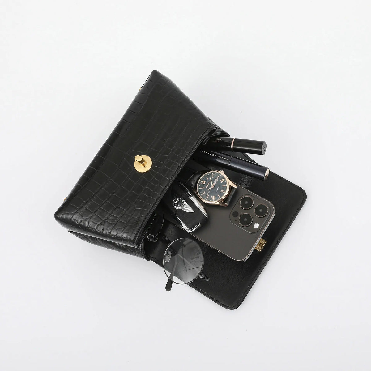 A black crocodile-embossed leather wallet organizer shown open on a white background, filled with a smartphone, watch, sunglasses, keys, and cosmetics.