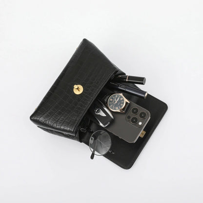 A black crocodile-embossed leather wallet organizer shown open on a white background, filled with a smartphone, watch, sunglasses, keys, and cosmetics.