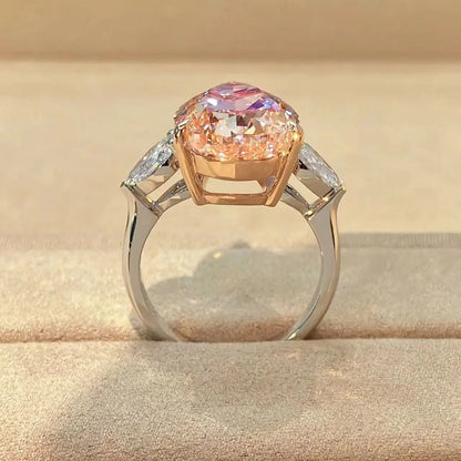 A ring with a large oval pink gemstone in a rose gold setting, flanked by two small clear stones on a polished silver-toned band, displayed on a beige textured surface.