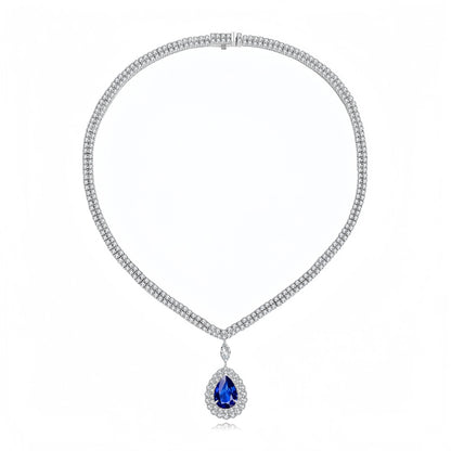 A silver-tone necklace featuring a textured chain paved with small clear stones, with a teardrop-shaped blue gemstone pendant surrounded by a halo of clear stones, shown on a white background.