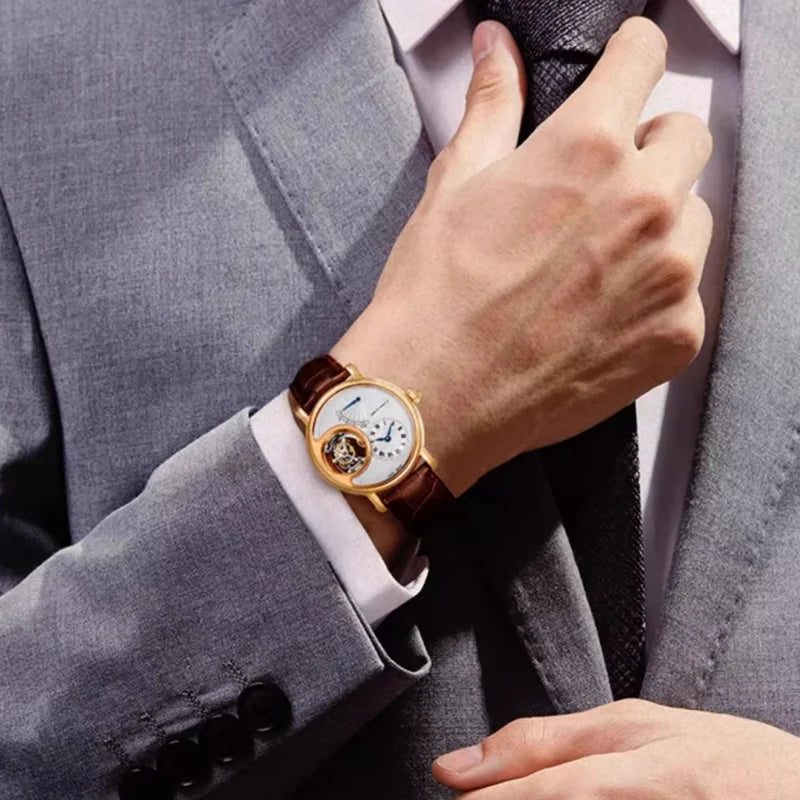A close-up of a man in a gray suit adjusting his tie while wearing a gold-tone wristwatch with a brown leather strap and a white dial.