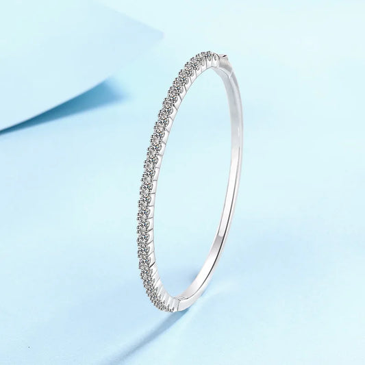 A slim silver-toned bangle bracelet with a single row of small clear stones, photographed on a light blue background.