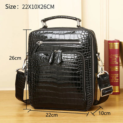 Black crocodile-embossed leather crossbody bag with top handle, front zip pockets, and adjustable shoulder strap, shown with overlaid dimensions 22x10x26 cm on a wooden surface with a book in the background.