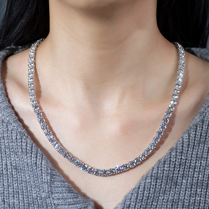 A close-up of a woman's neck and chest wearing a sparkling silver tennis-style necklace with clear stones, paired with a gray knit sweater.