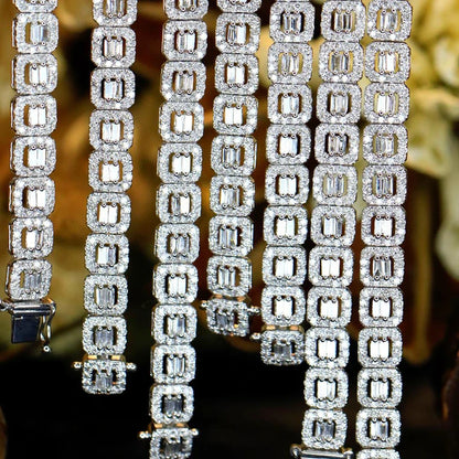 Close-up of multiple diamond-encrusted bracelet or necklace strands hanging vertically, featuring rectangular emerald-cut stones in silver-toned settings against a dark blurred background.
