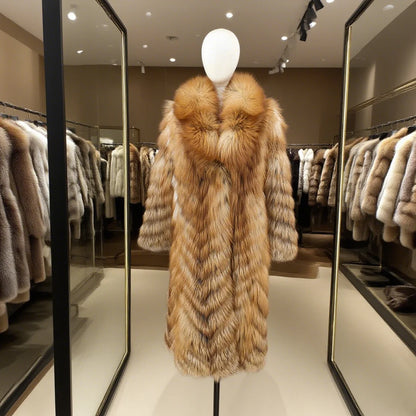 A long fur coat displayed on a white mannequin torso inside a boutique. The coat has a large shawl collar and wide sleeves, with a warm tan and cream fur pattern.