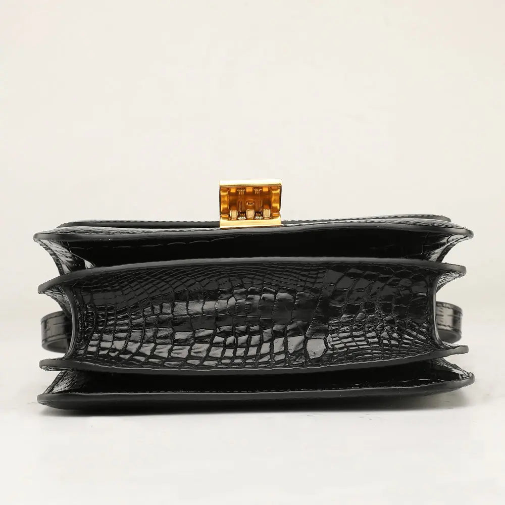 Black crocodile-embossed leather clutch bag with a gold-tone metal clasp, shown from the front on a light gray background.