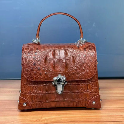 A brown crocodile-embossed leather handbag with a top handle, silver-tone hardware, and a decorative clasp, displayed on a wooden surface against a blue background.