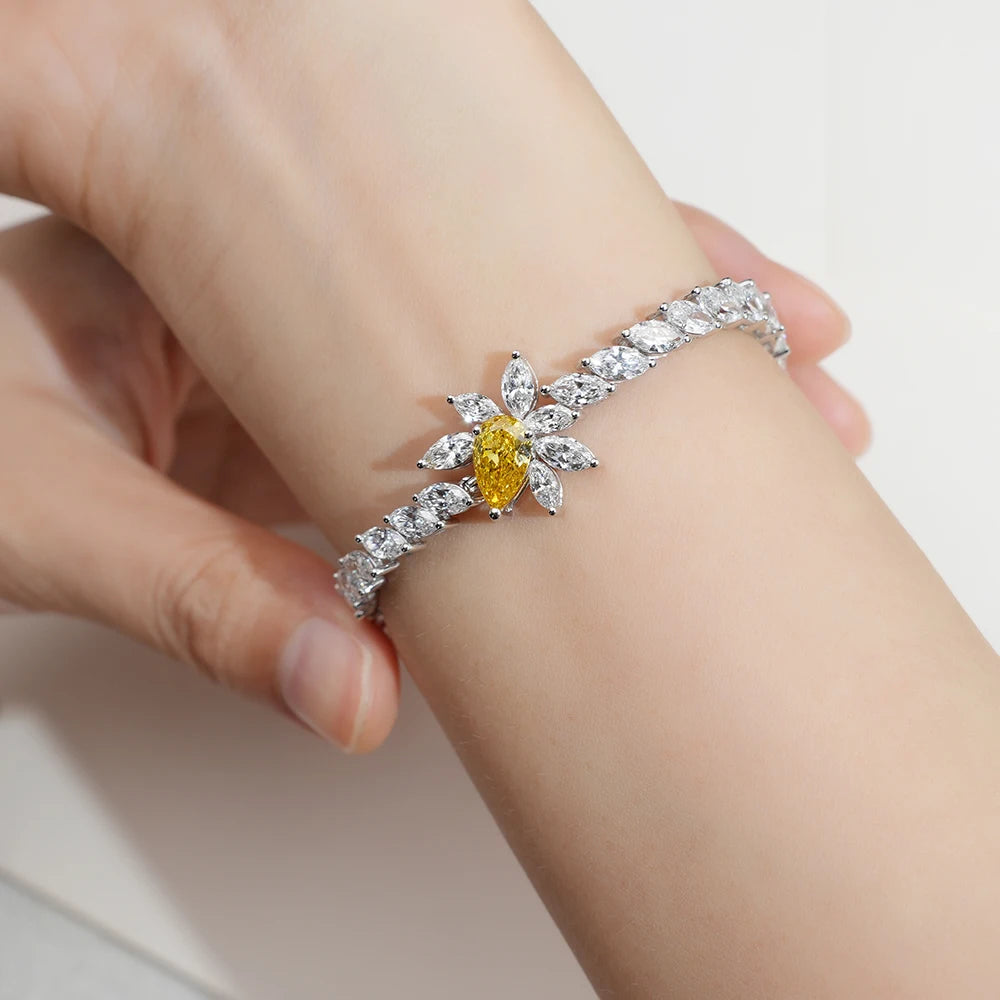 A close-up of a hand wearing a silver-toned flower-shaped bracelet with marquise-cut clear stones and a central yellow gemstone.