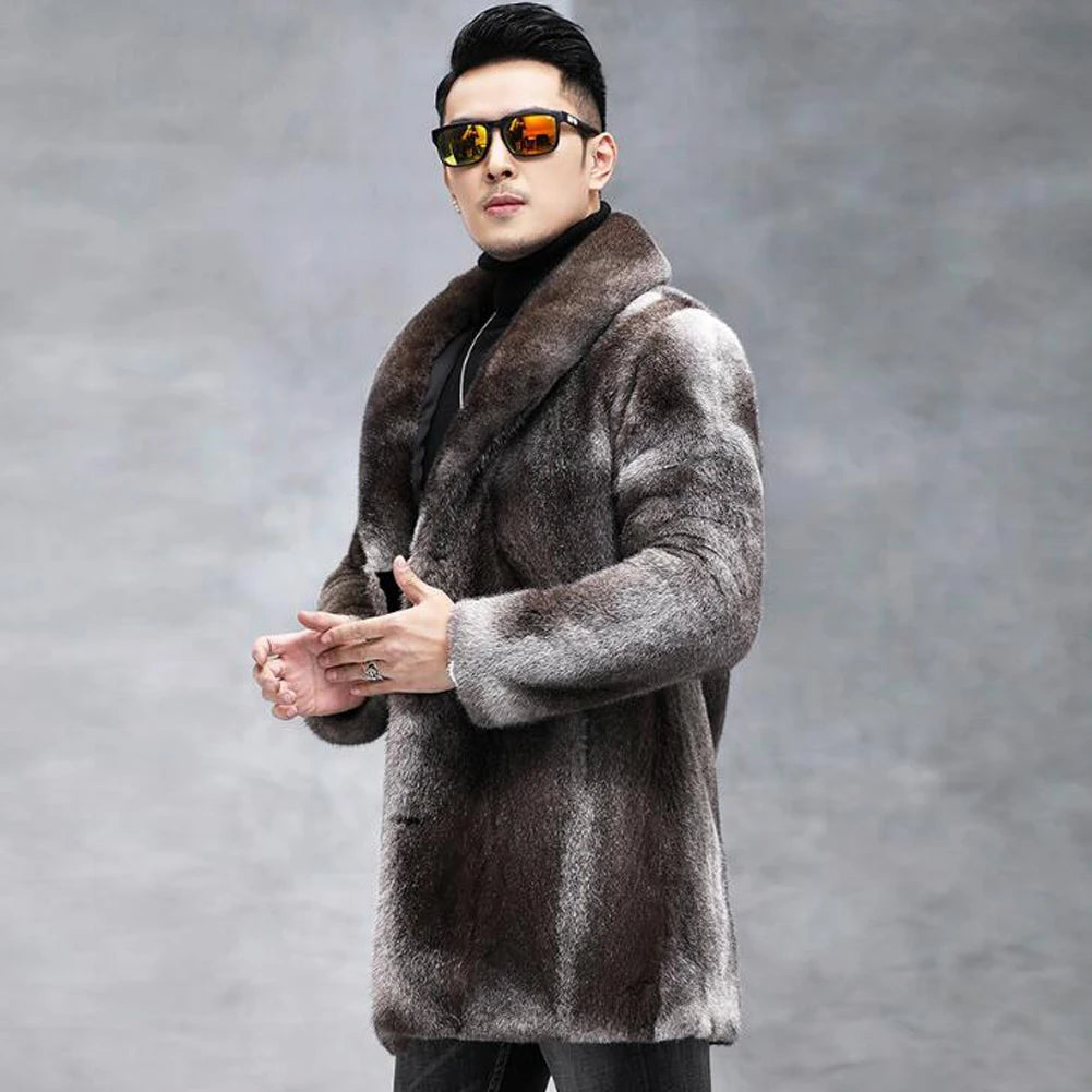 A man wearing a long brown and gray faux fur coat with a wide collar, black turtleneck, and black sunglasses with orange reflective lenses, posing against a gray studio background.