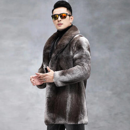 A man wearing a long brown and gray faux fur coat with a wide collar, black turtleneck, and black sunglasses with orange reflective lenses, posing against a gray studio background.