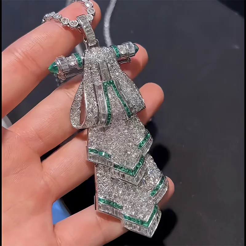 Elegant diamond and emerald pendant held in a hand against a dark background
