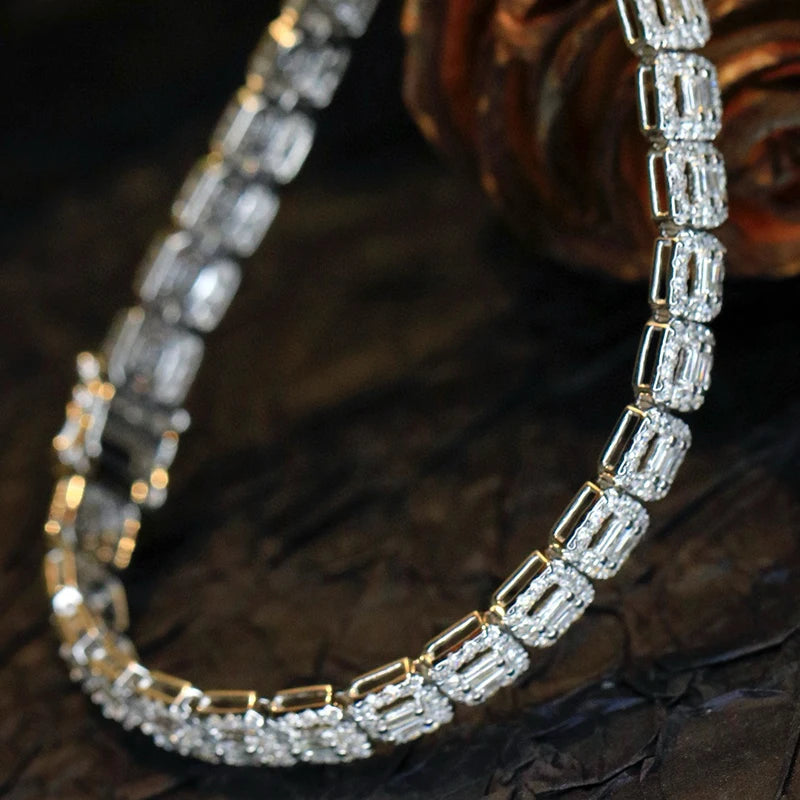 A close-up of a tennis-style necklace with rectangular clear stones set in yellow gold, arranged in a curved shape on a dark textured surface.