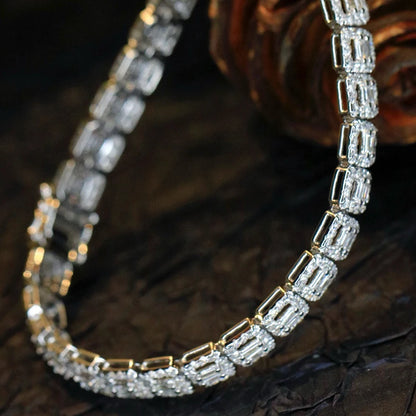 A close-up of a tennis-style necklace with rectangular clear stones set in yellow gold, arranged in a curved shape on a dark textured surface.