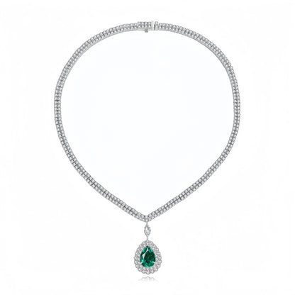 A white gold or platinum tennis necklace featuring a teardrop-shaped green emerald pendant surrounded by a halo of small clear stones, displayed on a clean white background.
