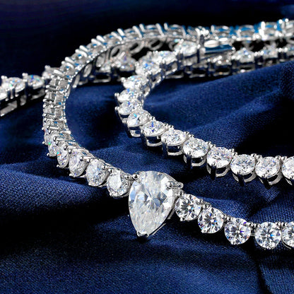 A close-up of a silver-toned tennis bracelet with a large pear-cut center stone and rows of clear round and marquise-shaped stones, displayed on dark navy blue fabric.