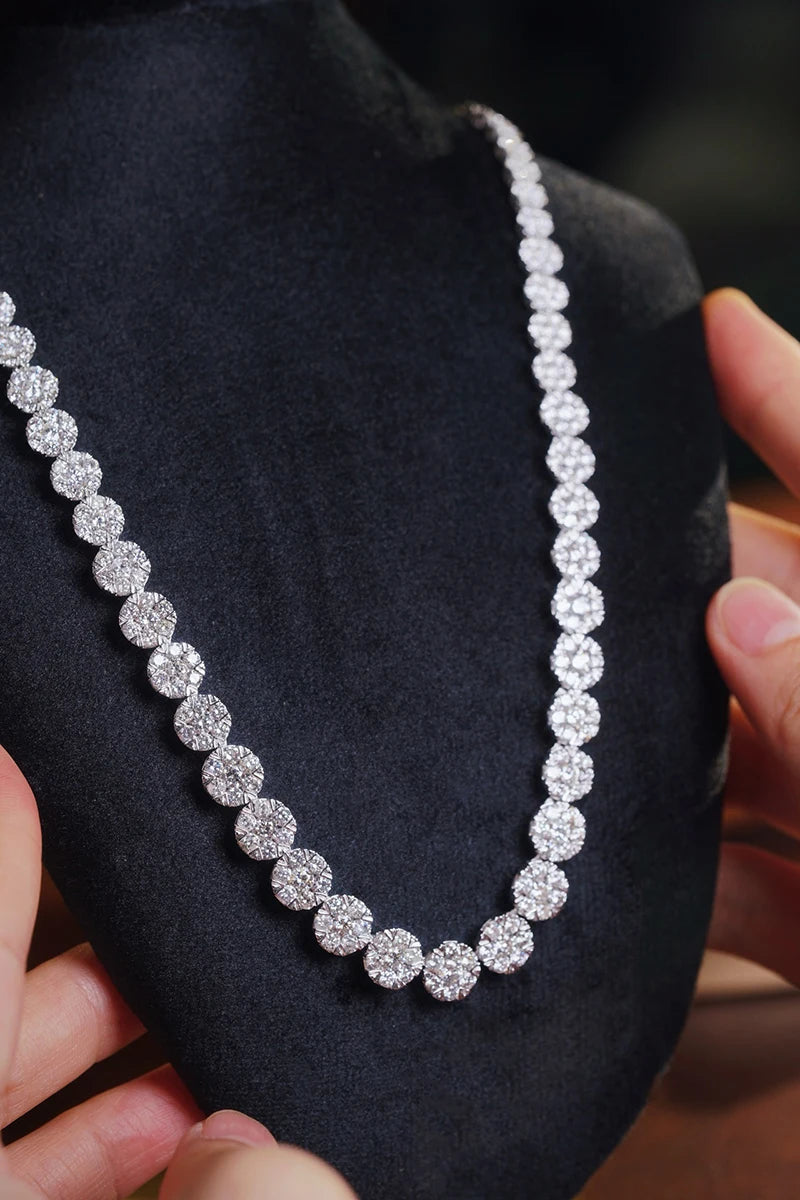 A sparkling silver-toned tennis necklace with round pavé-set clear stones, displayed on a black velvet jewelry bust with hands holding the sides.