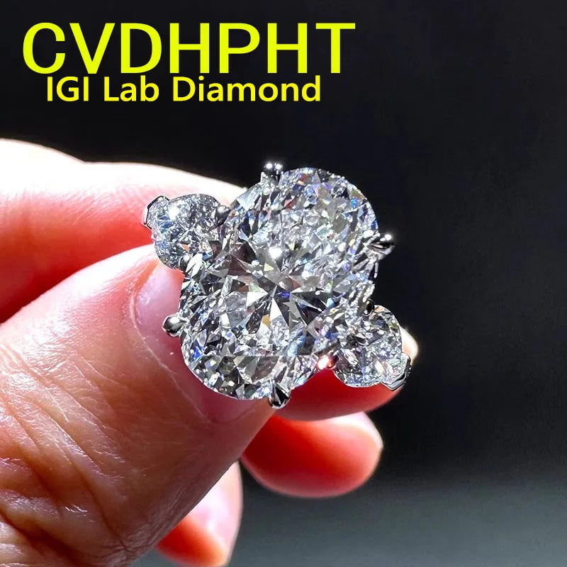 A close-up of a hand holding a large brilliant round diamond ring with smaller side diamonds, set in a silver-toned metal, against a dark background with yellow text reading 'CVDHPHT IGI Lab Diamond'.