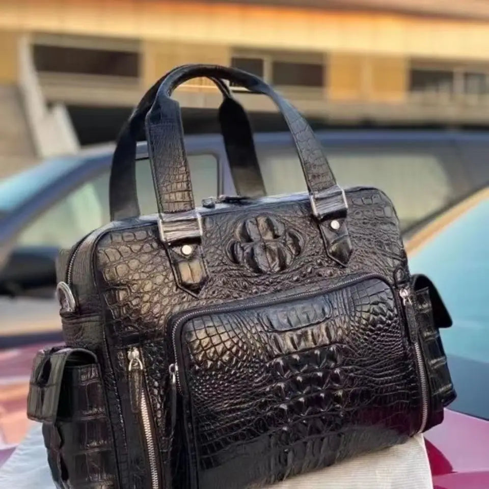 A black crocodile-embossed leather briefcase-style bag with dual top handles, front zip pockets, and side pockets, photographed outdoors on top of a car with a blurred background.
