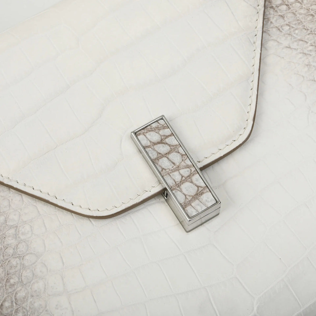 A close-up of a white textured leather clutch bag with a silver-toned metal clasp featuring a white and gray crocodile skin pattern.