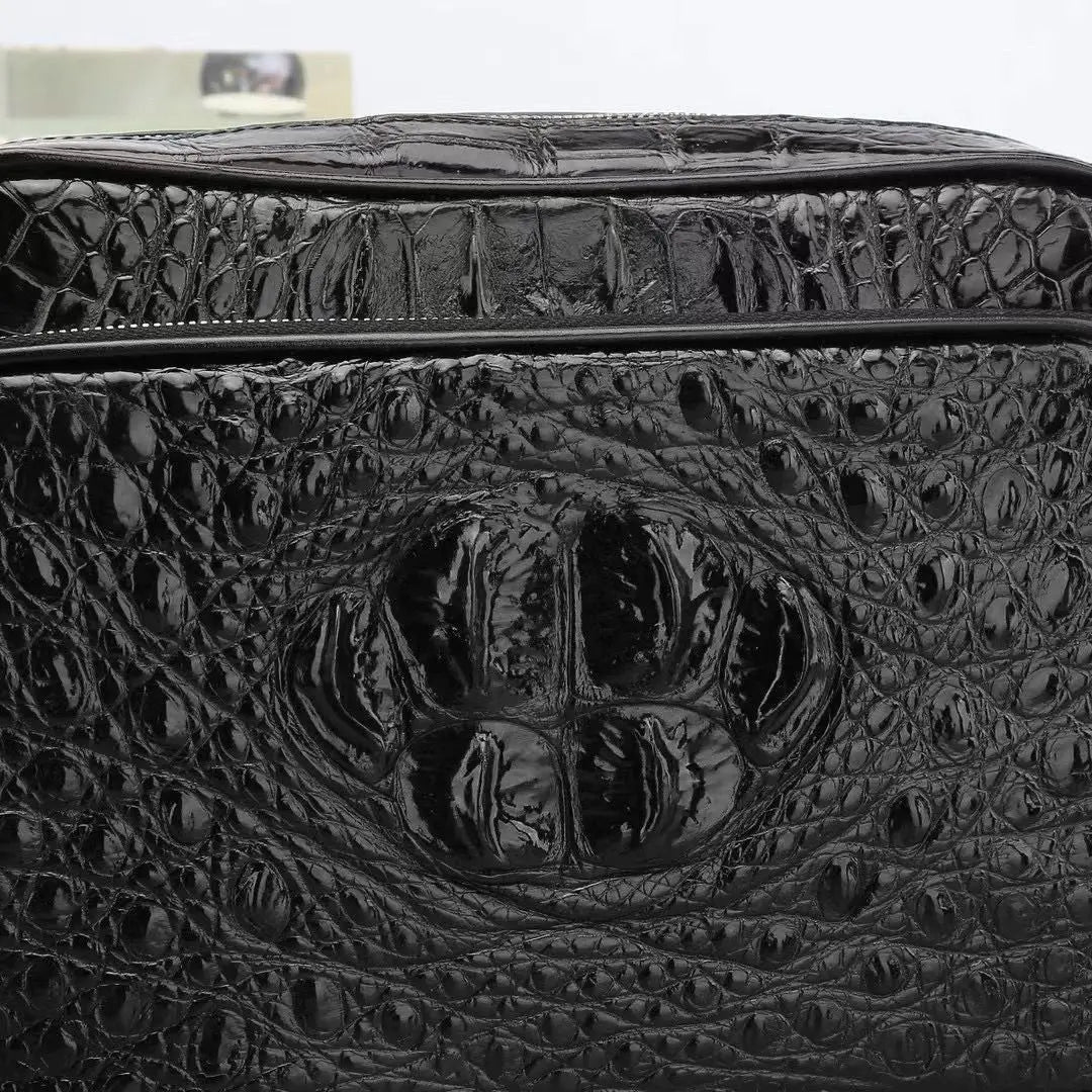 Close-up of a black crocodile-embossed leather bag or case, showing a glossy reptile texture and a central embossed motif.