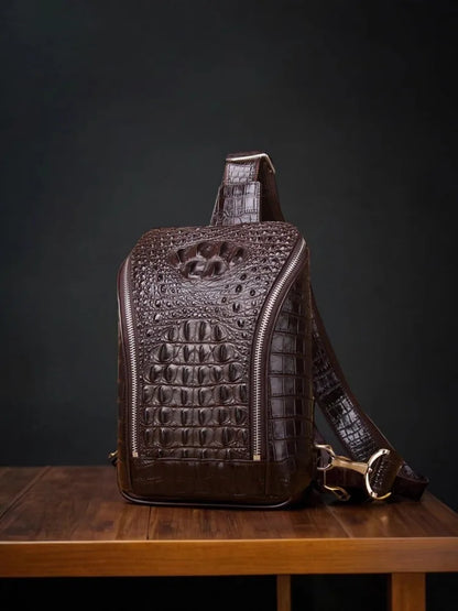 A dark brown crocodile-embossed leather backpack with gold-tone hardware, displayed on a wooden table against a dark background.