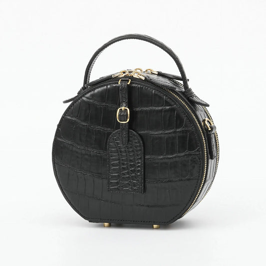 A black crocodile-embossed leather handbag with a top handle, gold-tone hardware, and a front luggage tag, shown on a plain white background.