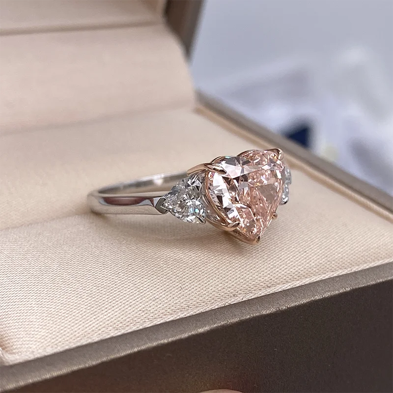 A heart-shaped pink gemstone ring with a silver band, displayed inside an open beige jewelry box.