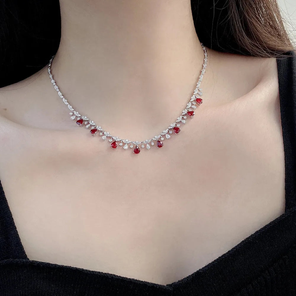 A delicate silver-toned necklace with small clear stones and red gemstone accents, worn on a model's neck over a black top.
