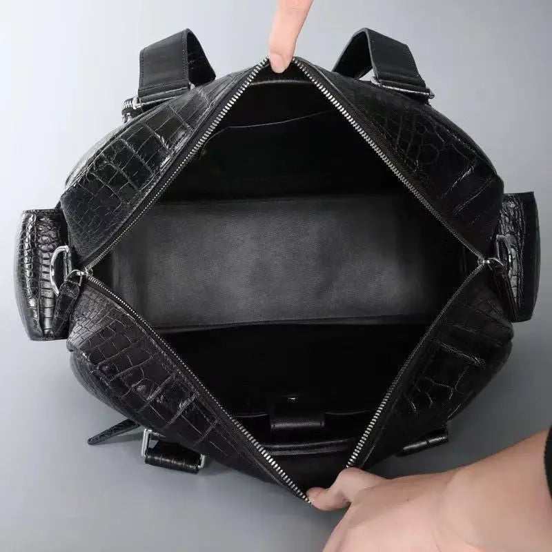 Black crocodile-embossed leather handbag shown open, with a finger pointing into the interior and hands holding the bag open at the top and bottom, against a plain gray background.