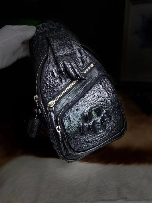 A black crocodile-embossed leather shoulder bag with gold-tone zippers, held by a white-gloved hand against a dark background.