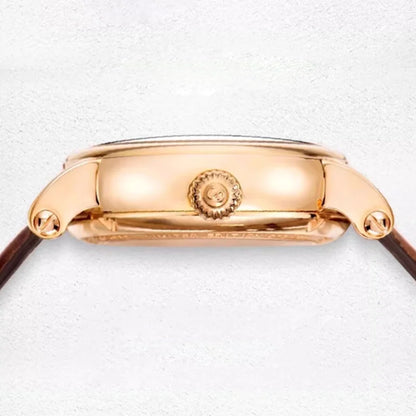Close-up of a rose gold watch case showing the crown and side lugs, with a dark brown leather strap visible on both sides against a light textured background.