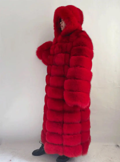 A person wearing a voluminous, bright red hooded fur coat with thick padded horizontal sections, standing against a plain off-white wall.
