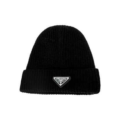 A black ribbed knit beanie hat featuring a small silver-tone triangular Prada logo patch on the front folded cuff, set against a plain white background.