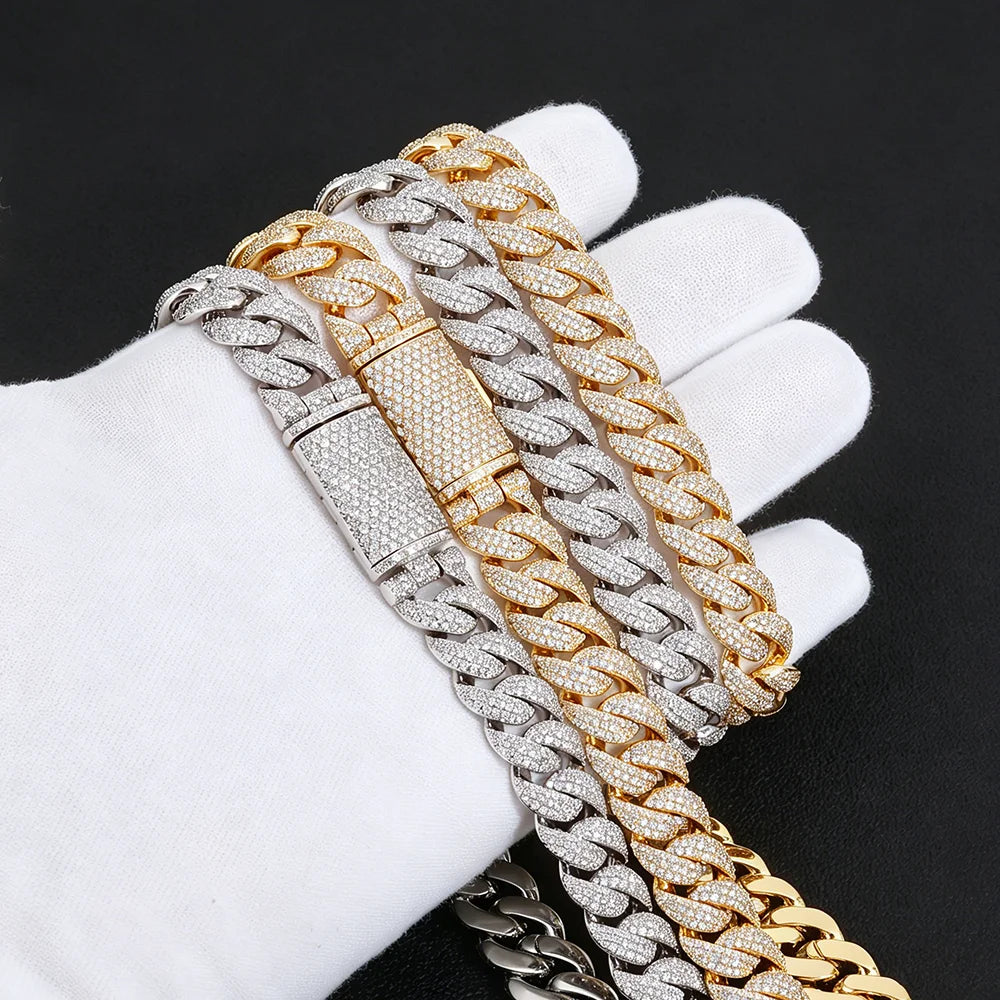 Three thick Cuban link chains with a diamond-like pavé finish, shown draped over a white gloved hand against a black background. The chains are in silver, gold, and a two-tone gold and silver combination.