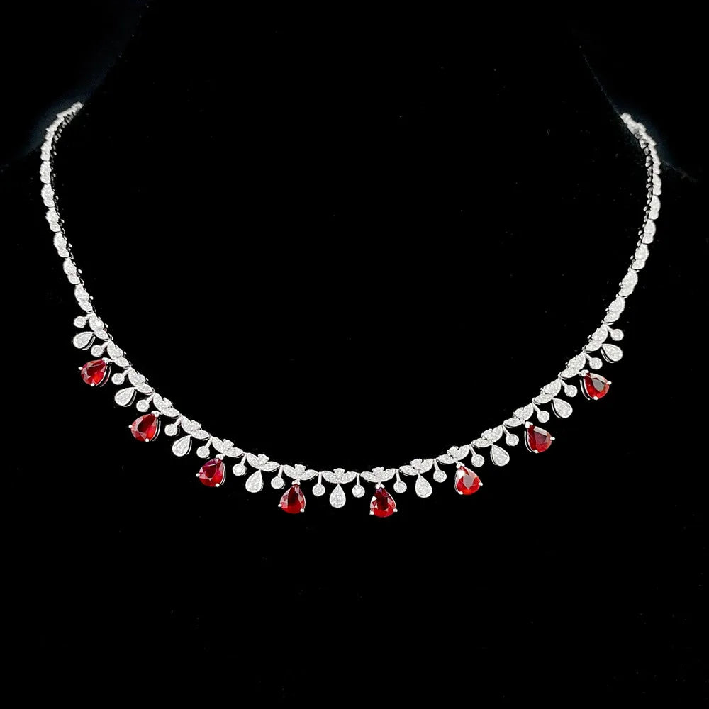 A silver-toned necklace with a row of clear teardrop-shaped stones and alternating red teardrop gemstones, displayed on a black background.