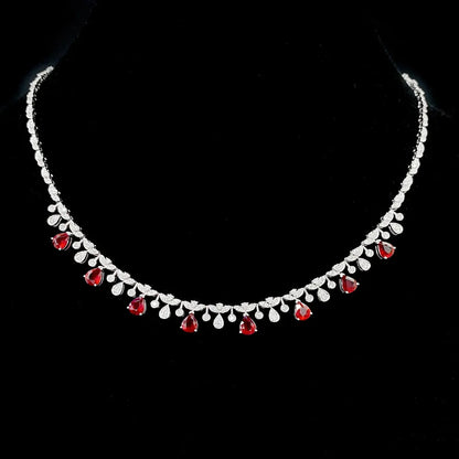 A silver-toned necklace with a row of clear teardrop-shaped stones and alternating red teardrop gemstones, displayed on a black background.