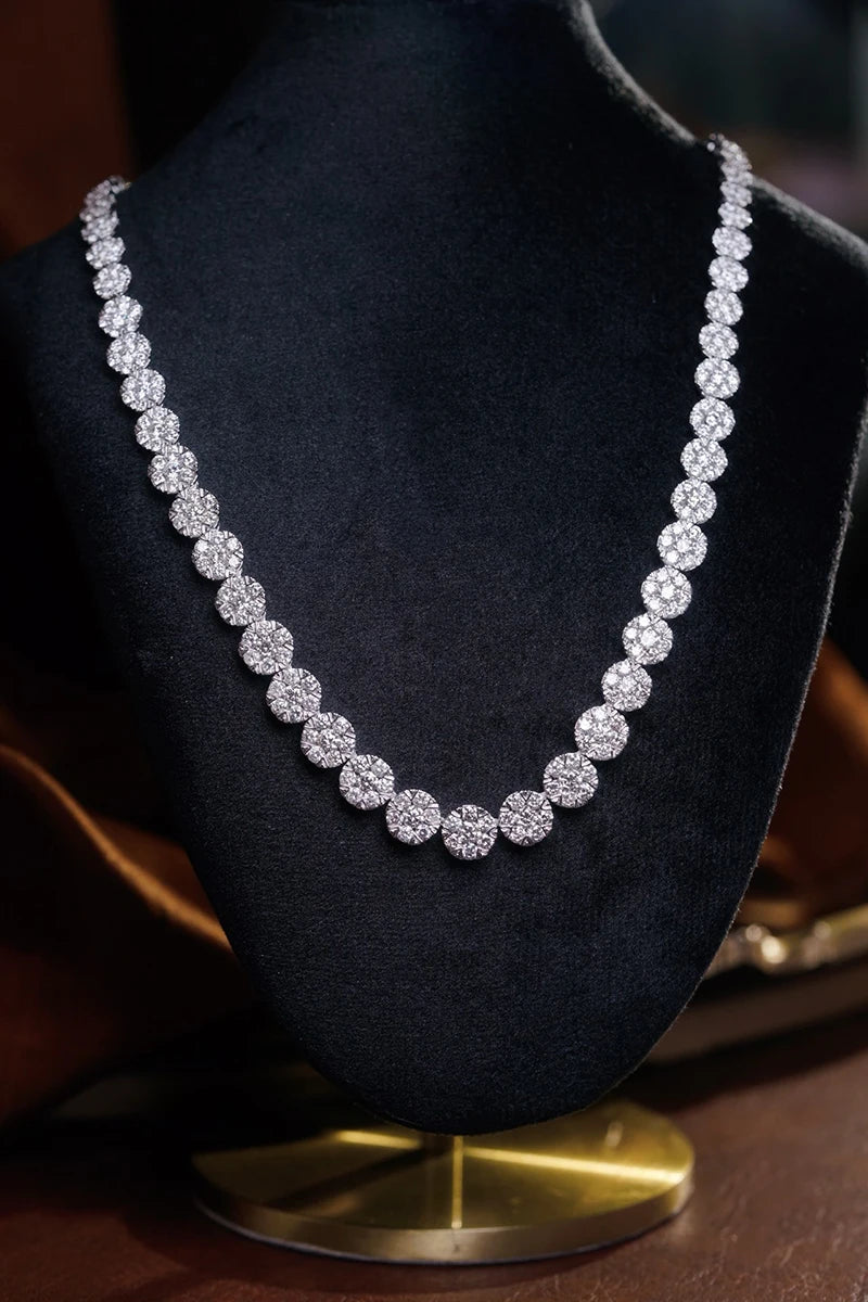 A sparkling diamond tennis necklace displayed on a black velvet jewelry bust with a gold base, set against a dark background.